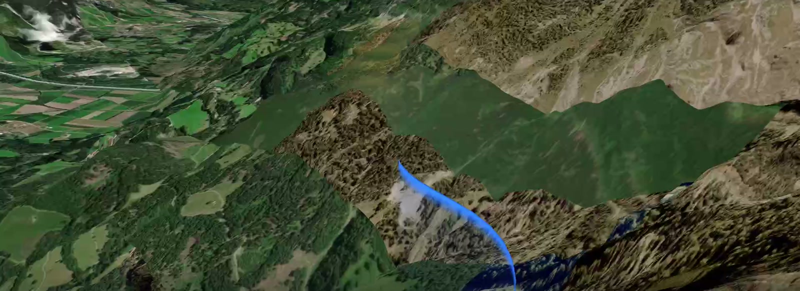 A glide descending into an alpine valley, the trail blue where the pilot is sinking